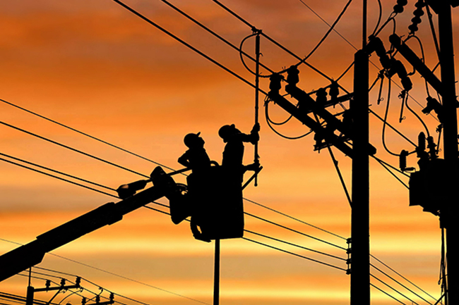 Utility workers working on electric distribution lines with a sunset back drop.